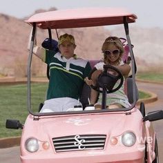 a man and woman are riding in a pink golf cart with the driver behind them