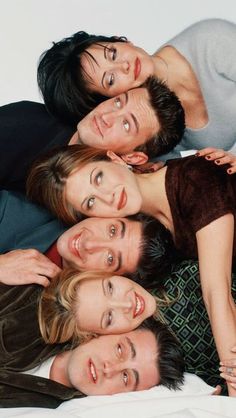 four people laying on top of each other with their arms around one another and looking at the camera