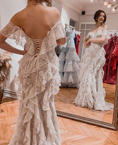 a woman is looking at herself in the mirror while wearing a wedding dress with ruffles