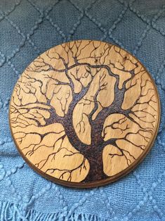 a wooden brooch with a tree on it sitting on a blue cloth covered surface