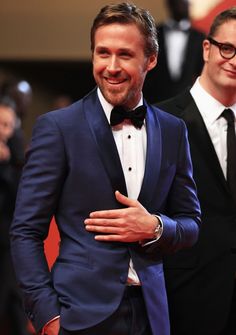 two men in tuxedos standing next to each other on a red carpet and smiling