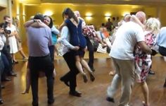 a group of people dancing on a wooden floor in a room with many other people