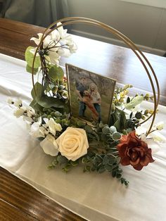 an arrangement of flowers and greenery on a table with a picture frame in the center