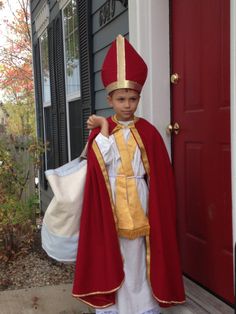 a young boy dressed in a red and gold priest's outfit, holding a white bag