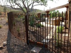 an iron fence is in the middle of a dirt area with trees and rocks around it