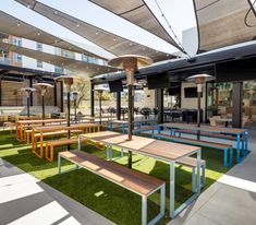 an outdoor seating area with wooden benches and tables on artificial grass in the foreground