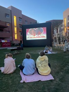 people sitting on the grass watching a movie in front of an apartment building at night