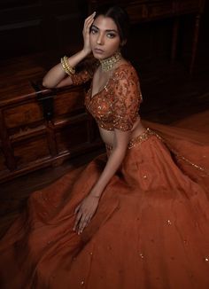 a woman in an orange dress sitting on the floor with her hand near her face