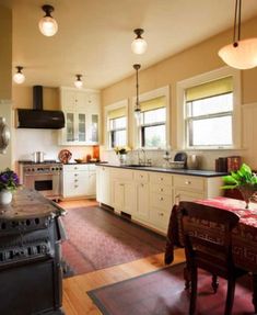 a large kitchen with white cabinets and wood flooring on the walls, along with a dining table set for four