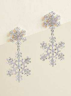 two snowflake earrings are hanging from a white wall and one is wearing a silver necklace