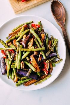 a white plate topped with green beans and red bell peppers next to a wooden spoon