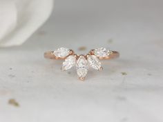 a rose gold ring with three pear shaped diamonds on the top and bottom, in front of a white flower