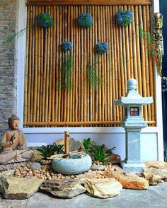 there is a buddha statue sitting in front of a bamboo wall with succulents on it