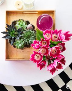 pink flowers and succulents in a wooden tray on a white table with black and white checkered flooring