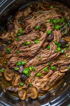 a slow cooker filled with beef and mushrooms, garnished with scallions