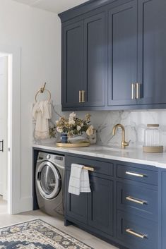 a washer and dryer in a kitchen with marble counter tops, blue cabinets and gold handles