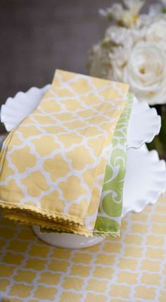 two yellow and green napkins sitting on top of a white plate next to flowers