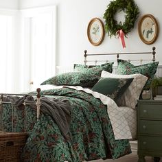 a bed with green and red comforters in a room next to a dresser, two wreaths on the wall