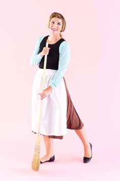 a woman in an apron holding a broom and posing for the camera on a pink background