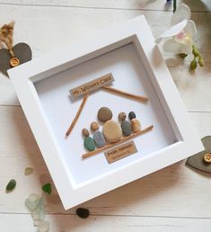 a white frame with rocks and wooden sticks in it on a table next to flowers