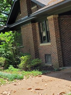 a cat sitting on the front porch of a brick house with trees in the background