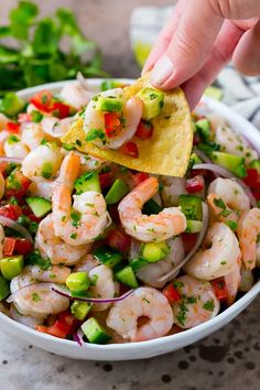 a hand dipping a tortilla chip into a bowl of shrimp salad