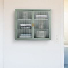 a green cabinet sitting on the side of a white wall next to a window with glass doors