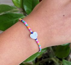 a woman's arm with a colorful bracelet and heart shaped bead on it