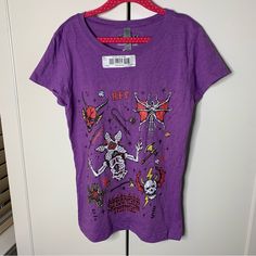 a purple t - shirt with cartoon images on it is hanging from a hanger