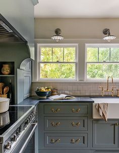 a kitchen with gray cabinets and white counter tops, two windows above the stove top