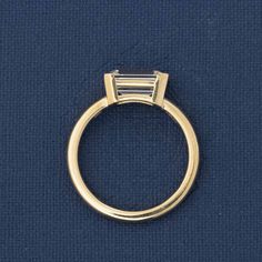 a yellow gold ring with two baguetts on the top and bottom, against a blue background