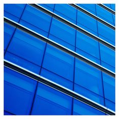 the side of an office building with blue glass on it's windows and sky in the background