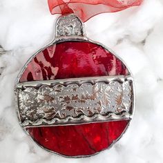 a red glass ornament hanging on a white marble surface with a red ribbon around it