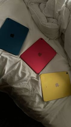 three different colored laptops sitting on top of a white bed next to each other