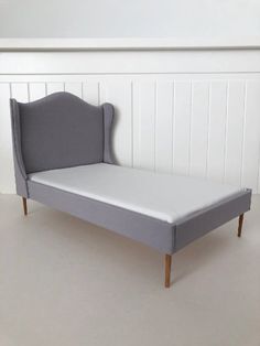 a gray bed frame with wooden legs and headboard on the bottom, in front of a white wall