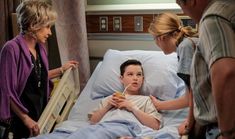 a young boy laying in a hospital bed being examined by an adult and three other people