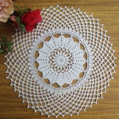 a crocheted doily on a wooden table next to a flower vase with red roses