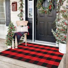 the front porch is decorated for christmas with wreaths and pine trees on the door mat