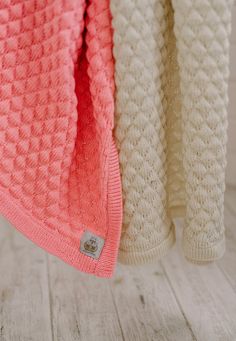 two knitted sweaters hanging on a clothes line, one in pink and the other in white