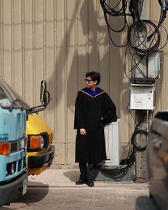 a man standing in front of a building wearing a graduation gown and sunglasses with his hands on his hips