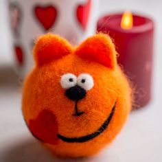 an orange stuffed animal with a heart on it's face next to two candles