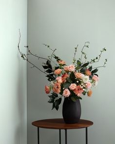 a black vase with pink and white flowers on a small table in front of a wall