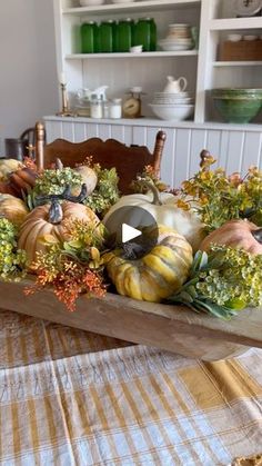 a wooden tray filled with pumpkins and greenery on top of a dining room table