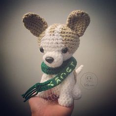 a small crocheted dog with a green scarf around its neck is being held by someone's hand