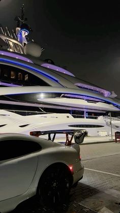 a white sports car is parked in front of a large yacht at night with its lights on