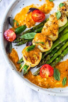 grilled shrimp and asparagus with tomato sauce on a white plate, ready to be eaten