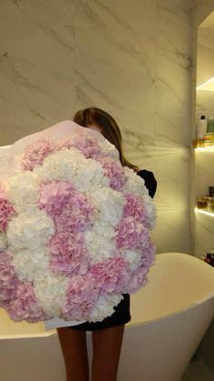 a woman holding a giant bouquet of flowers in front of a bathtub with shelves behind her