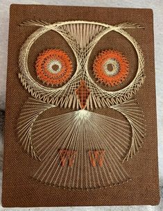 an owl made out of yarn on top of a piece of brown paper with orange eyes