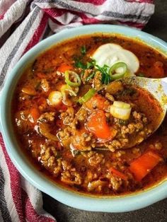 a bowl of soup with meat, carrots and sour cream on the spoon in it