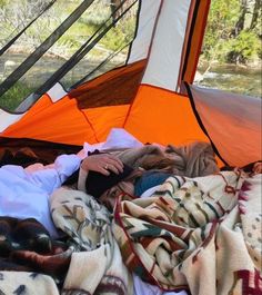 a person laying in a tent with blankets on the ground and an orange tarp over them